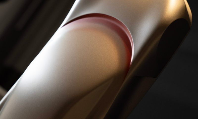 A dynamic photo of a Karma Kaveya speedform finished in Electrum Gold with red paint trimming the inside of the comet line.